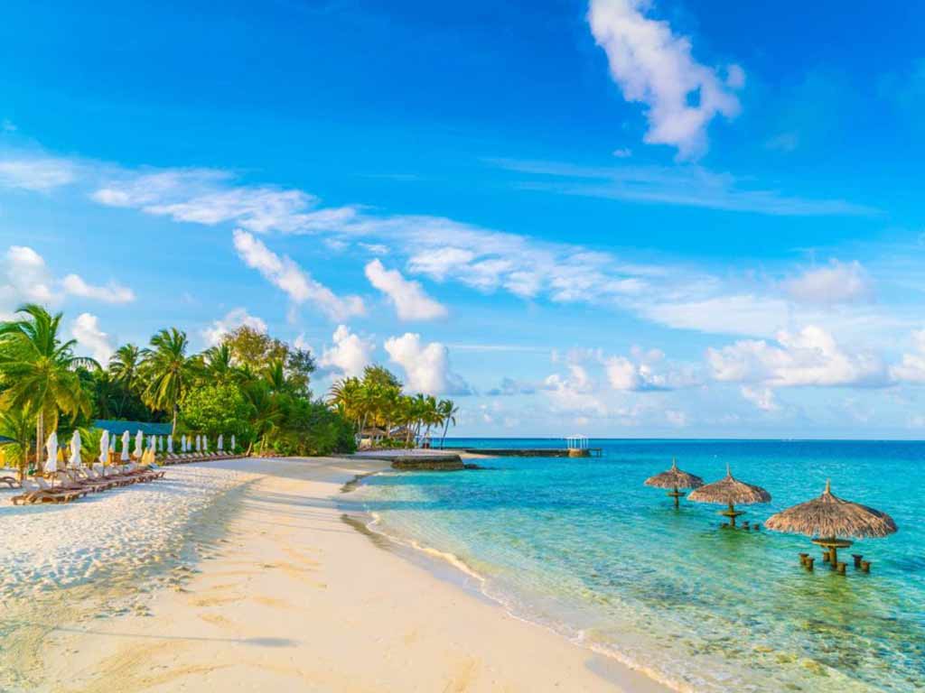 A beautiful island in Maldives with white sandy beaches and clear waters and some wooden stools and shades placed in the water to relax