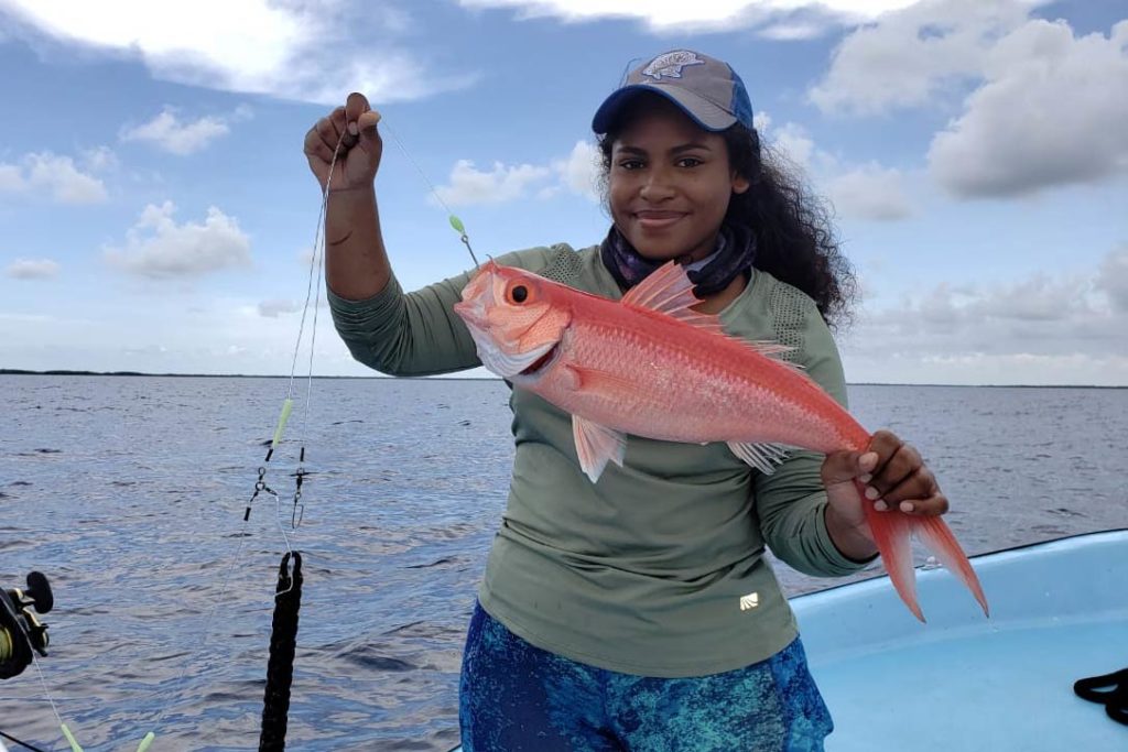 A female angler in a cap holds a Caribbean Queen Snapper caught on the reefs while standing on a boat