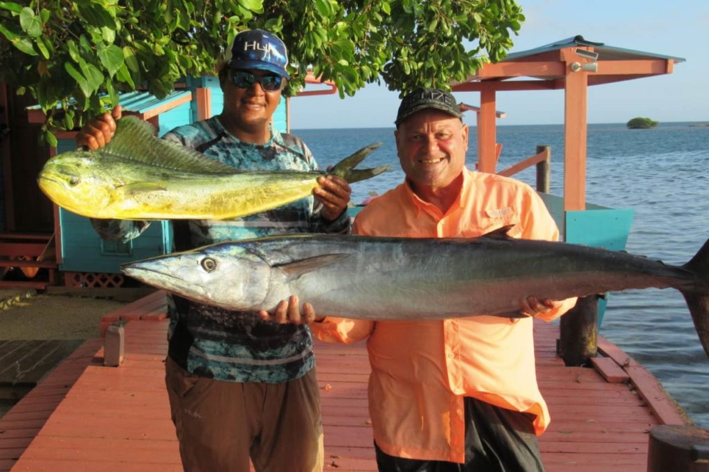 Two anglers hold a Mahi Mahi and Mackerel caught on a Belize fishing trip, while standing on a wooden board