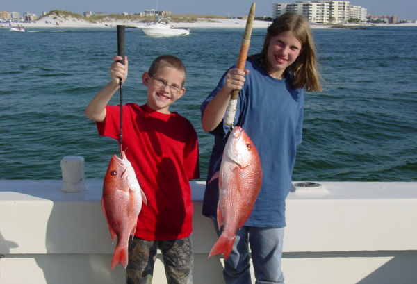 A boy and a girl on a charter fishing boat holding up the Red Snapper they caught