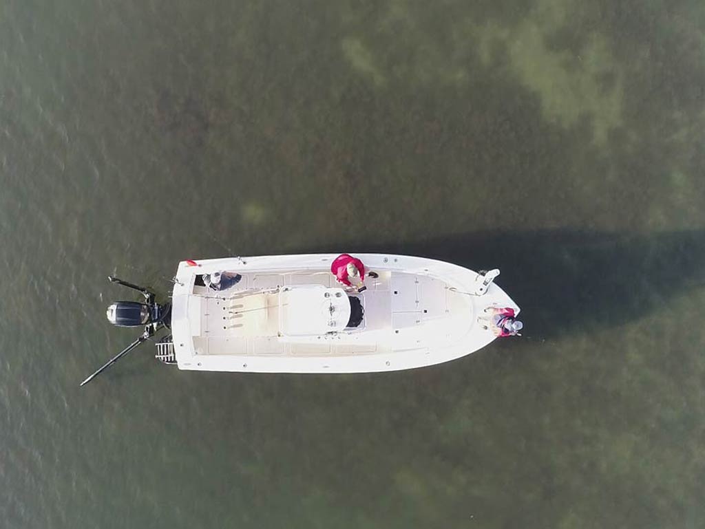 An aerial view of a charter boat, a center console, on murky waters, directly from above it, with three anglers on the boat fishing.