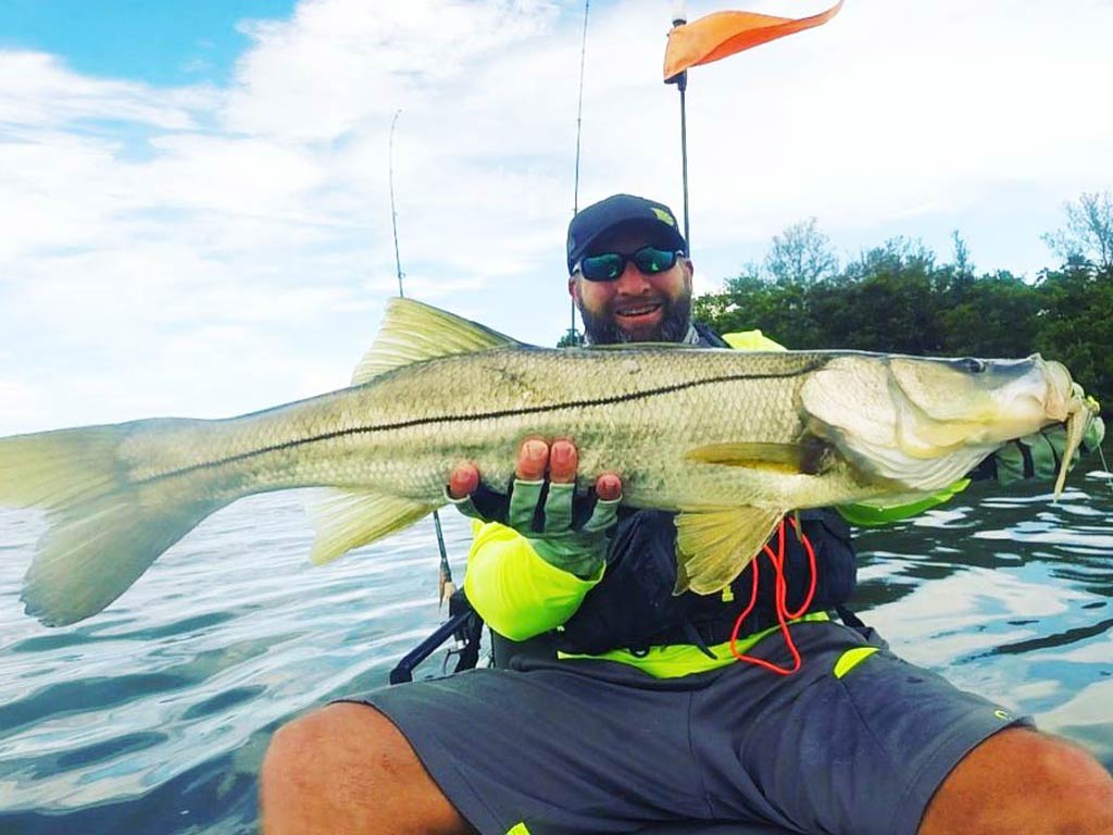 A kayak angler holding a big Snook while sitting in a kayak on the waters of Tampa Bay