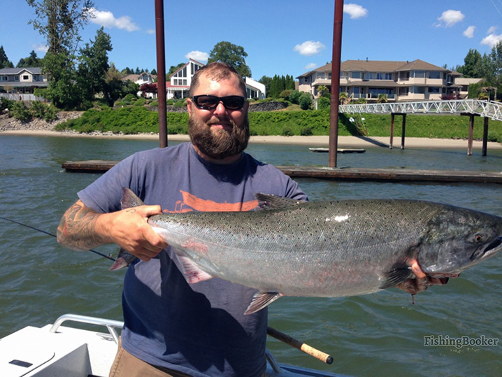 A man holding Salmon aboard a fishing charter in Portland Maine on a sunny day with Portland in the background.