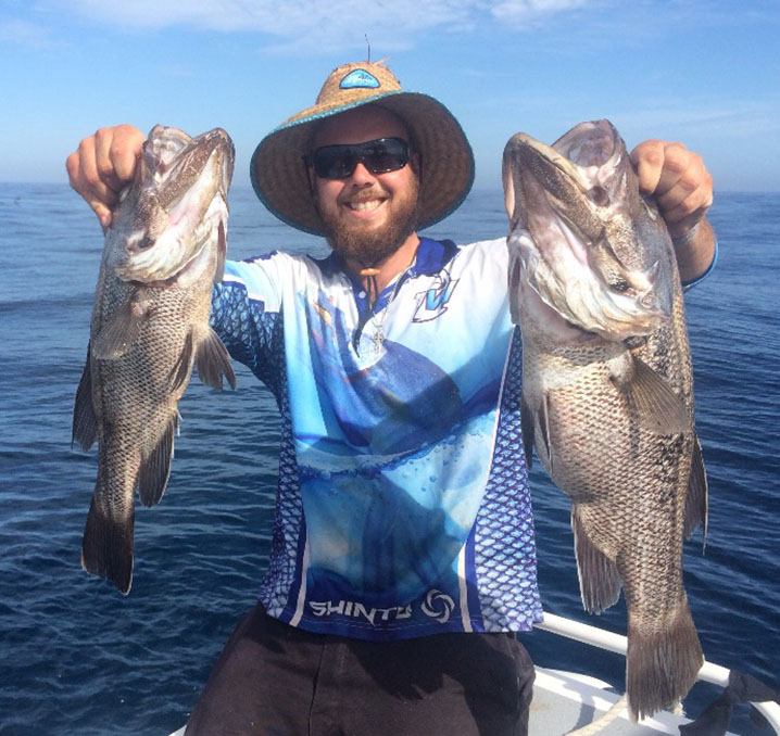 A smiling angler holding two Dhufish he caught when fishing near the Abrolhos Islands in Western Australia.