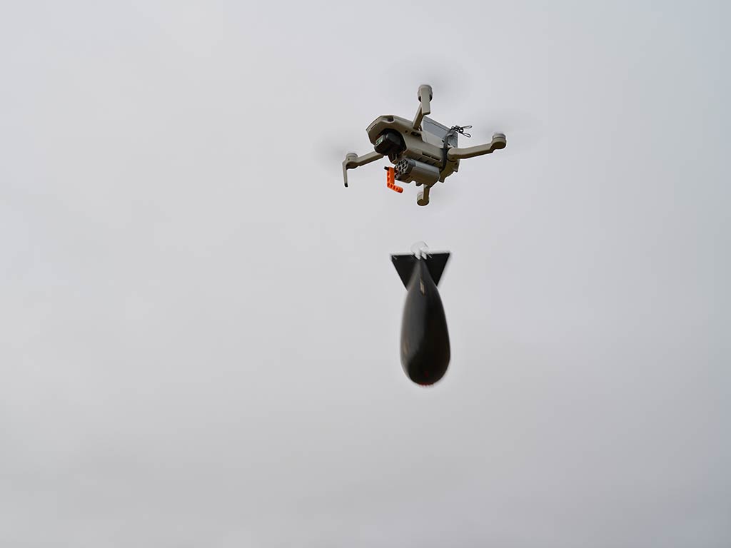 A drone, designed for fishing, is soaring through the clear sky while it’s carrying a small bomb.