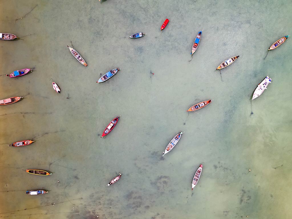 An aerial view showing multiple small boats scattered across clear, shallow water in vibrant hues.