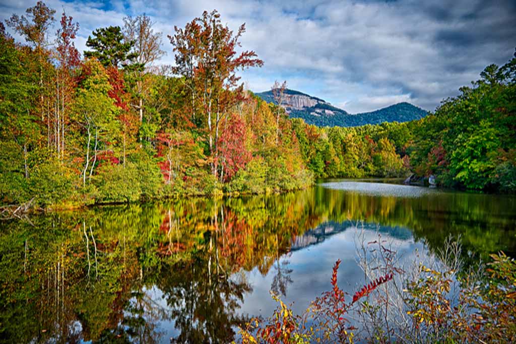A stunning view of Lake Jocassee, one of the best family fishing destinations in South Carolina, in fall, with colorful trees reflecting off the calm water surface