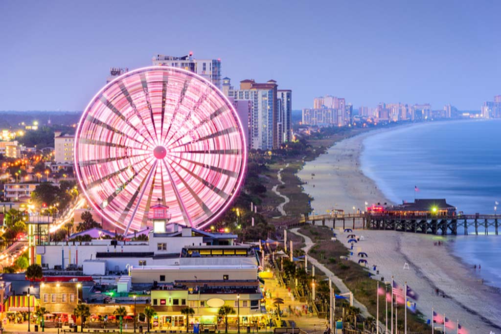 A view of the ferris wheel in Myrtle Beach at sunset, with the beach and the ocean visible to the right of the wheel