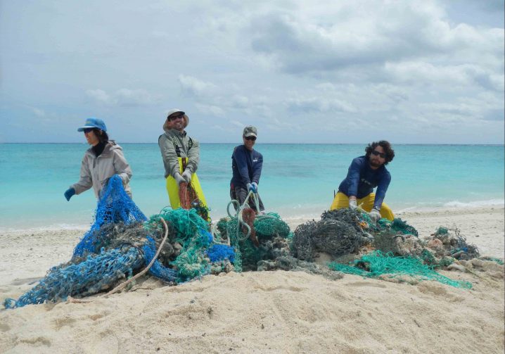 Four people standing on a beach with a pile of ghost fishing nets they removed from the sea