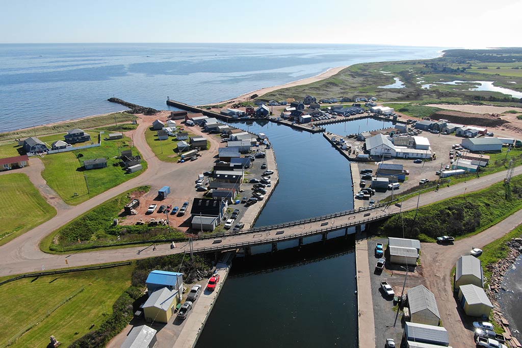 An aerial view of a harbor and river leading into North Lake on Prince Edward Island on a clear day with a bridge visible in the foreground