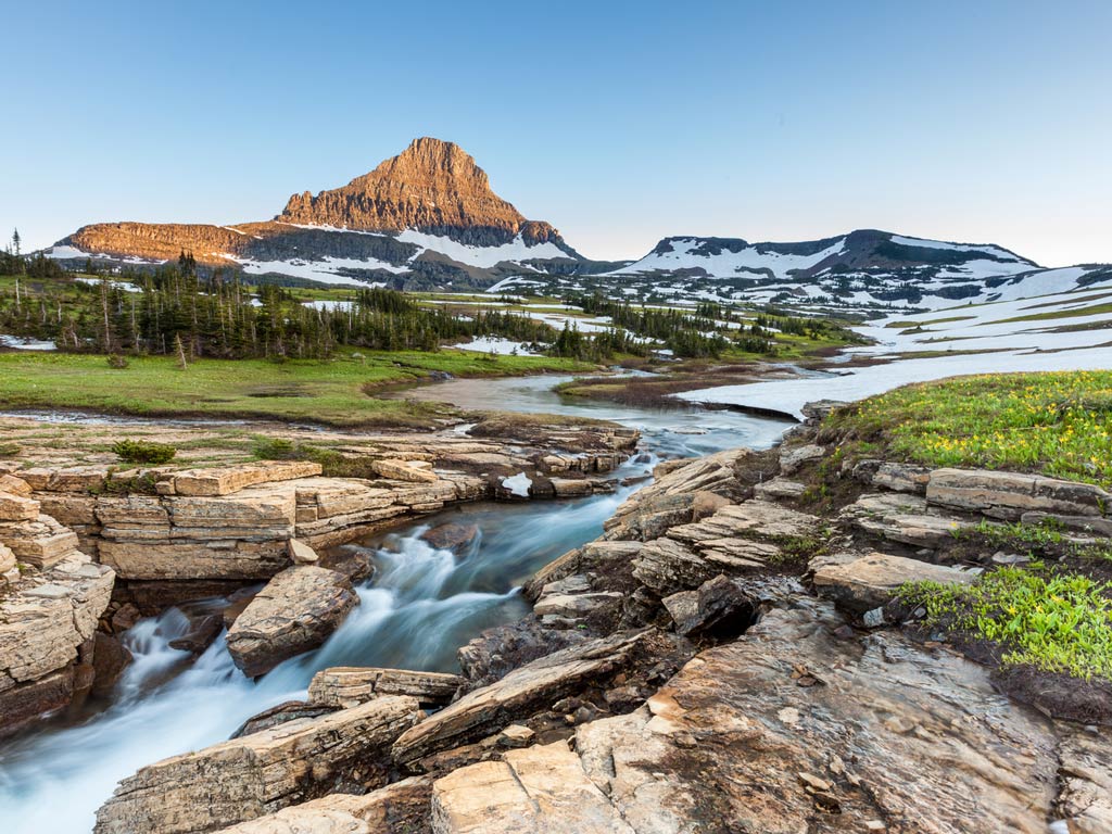 A beautiful view of the rocks, greenery, and snow-covered hills and a mountain in the distance in Logan Pass, Glacier National Park