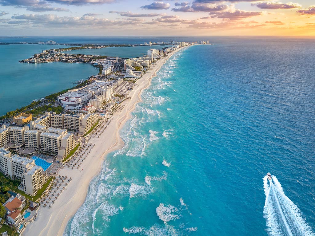 An aerial view of the resorts on Cancun, Mexico's Zona Hotelera, with a boat in the sea on the right.