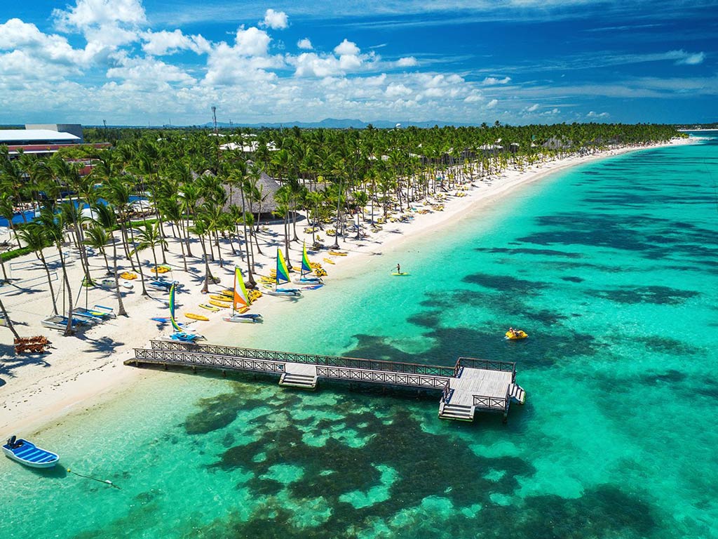 A view from above of the beach at Punta Cana, Dominican Republic, with palm trees and a small pier going into the water.