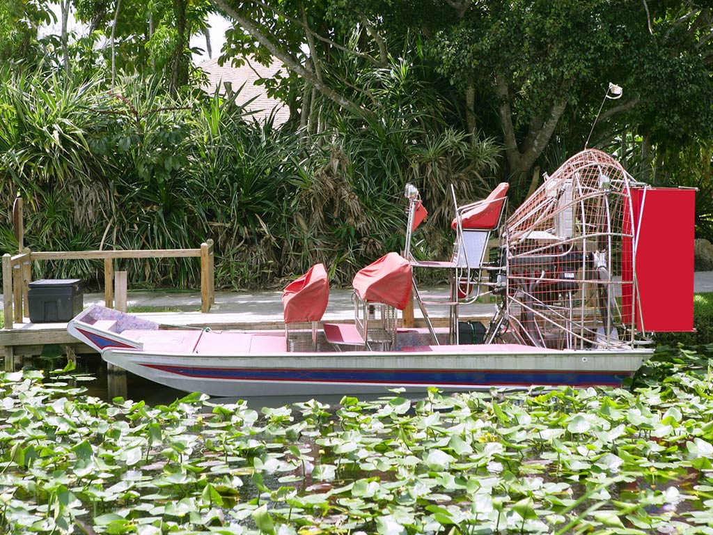 A side view of an airboat docked next to a small wooden pier 