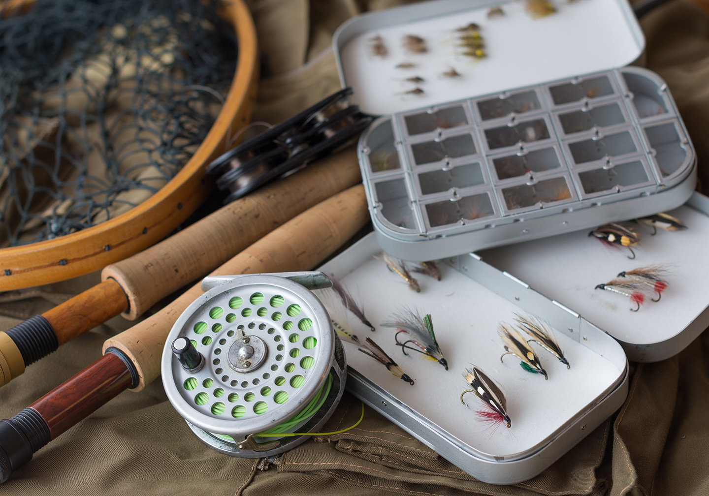 A selection of different fly fishing gear, including a reel, two rods, a net, and a selection of fishing flies.