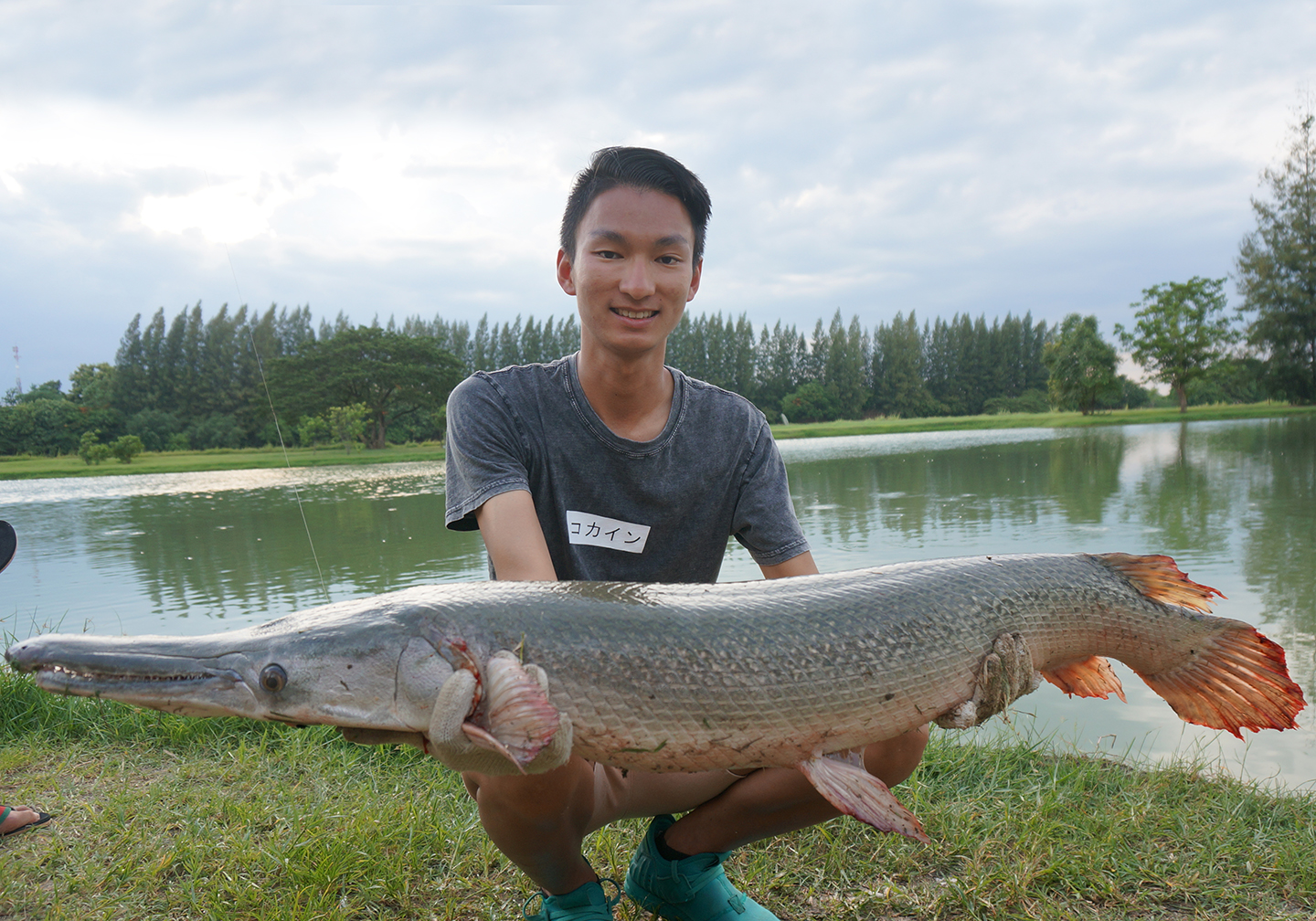 A happy angler crouching by the side of a lake holding an Alligator Gar fish.