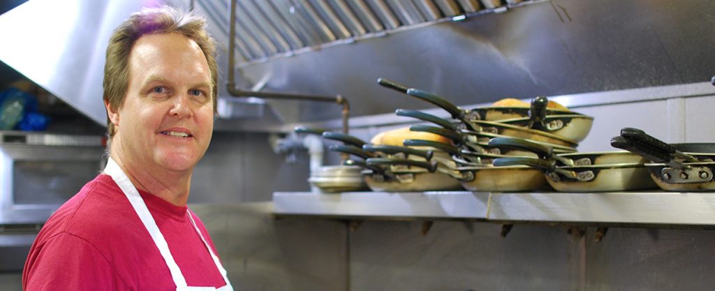 Chef Frank at Frank's Grill in the kitchen with pans on a shelf next to him