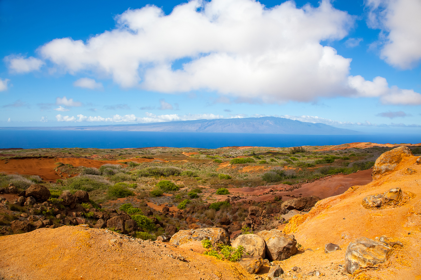 A view across dry land towards the sea on the island of Lanai, Hawaii, with the island of Maui in the distance.