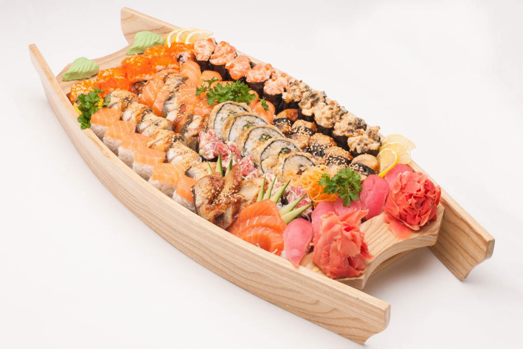 A wooden sushi platter filled with all kinds of sushi, arranged in an appetising manner, on a white background.