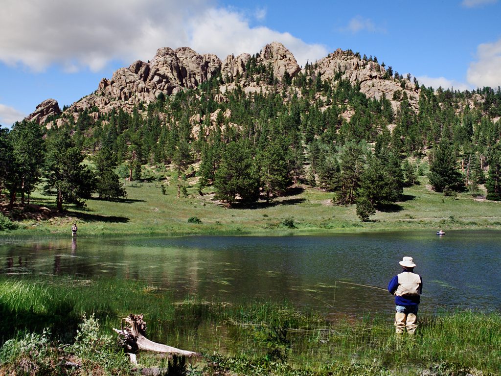 A view behind of a man fishing in the Rocky Mountains on a clear day.