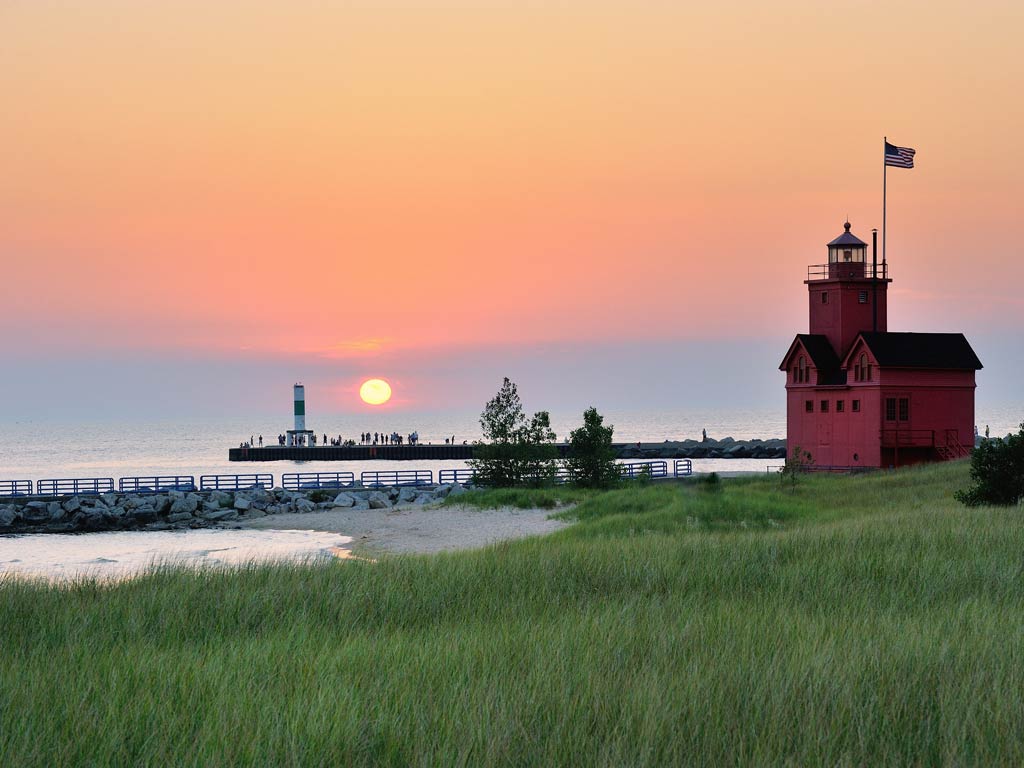 A red barn in Holland, MI, with green grass and a red sunset in the distance