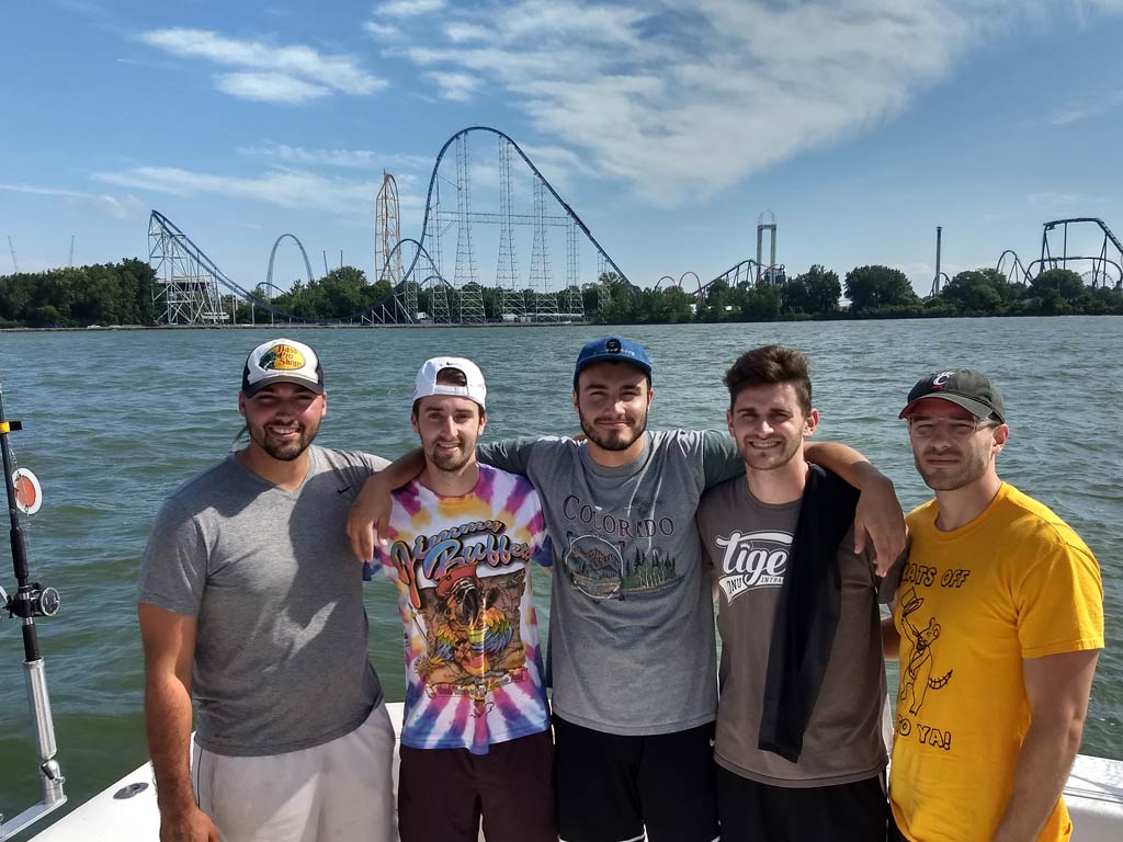A group of anglers on a charter fishing boat, with the rollercoasters of Sandusky in the distance behind them