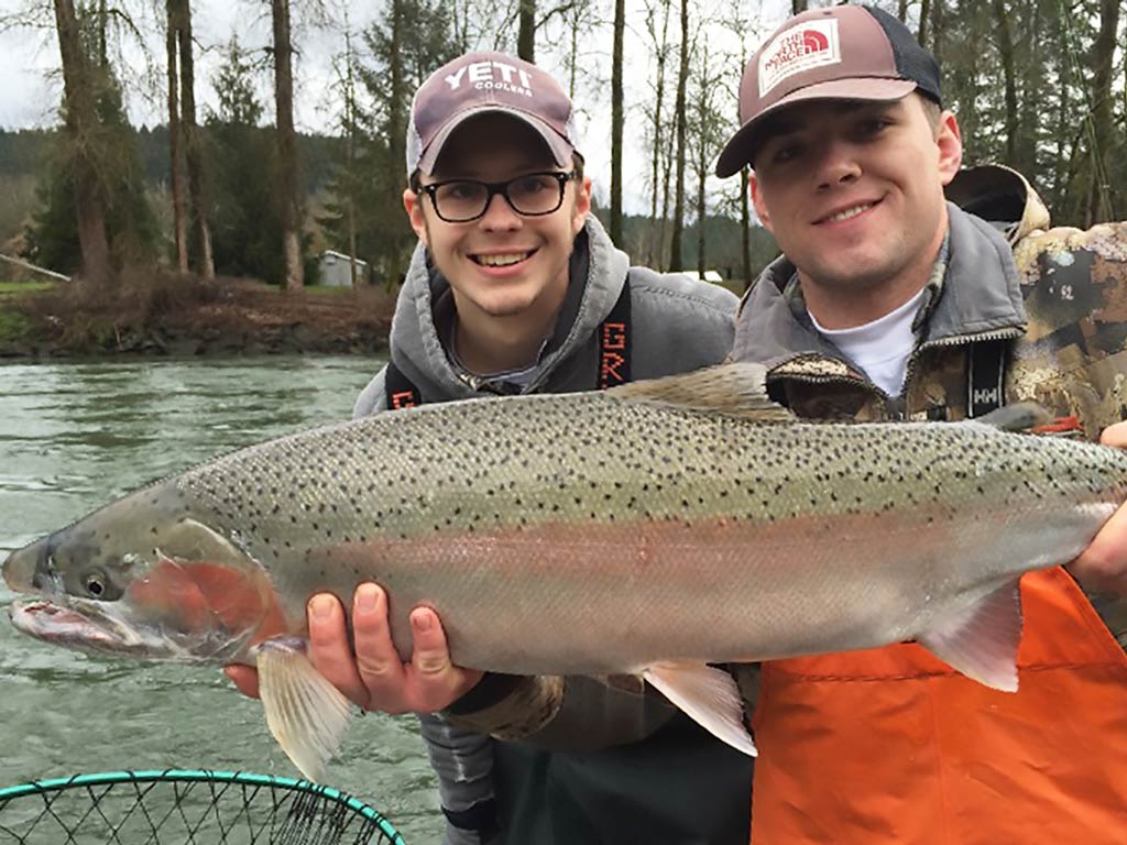 A photo featuring two anglers on a fly fishing trip in Oregon posing with a big Steelhead Trout caught during the fall fishing season.