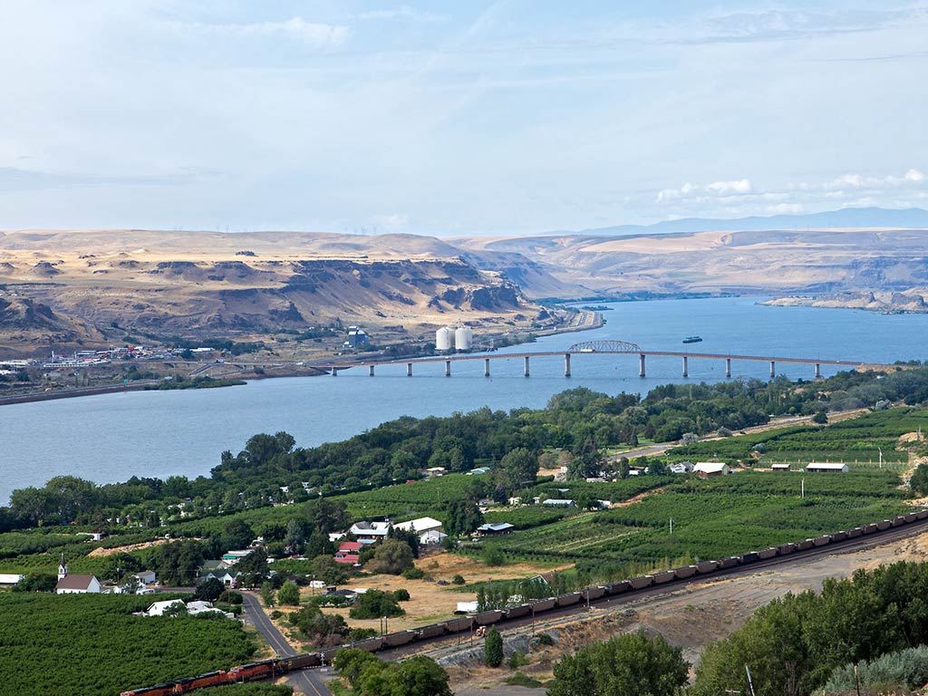 Scenic view of the Columbia River with a bridge crossing over it, surrounded by lush green farmland perfect for Oregon fly fishing in the foreground. 