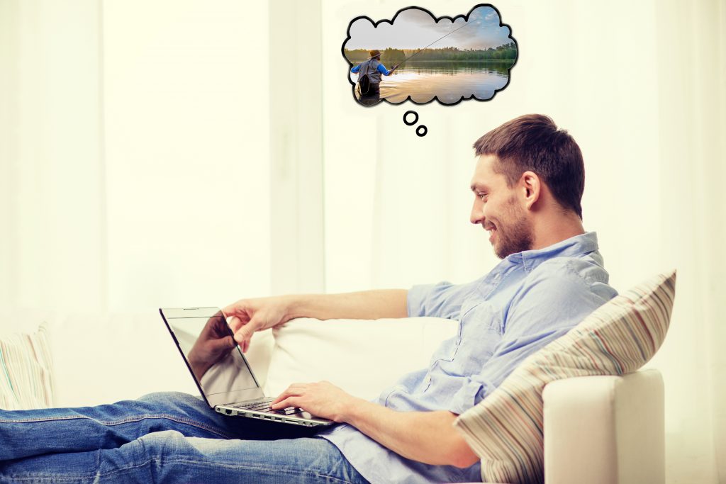 A man sitting on the couch with a laptop, thinking about fishing