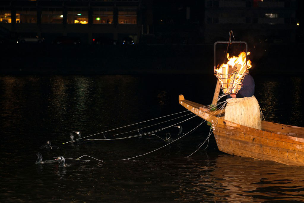 Cormorant fishing in the middle of the night with a boat to the right, Japan