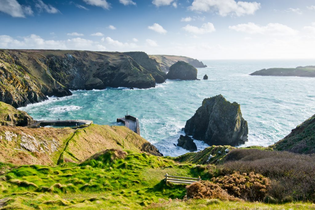 A sunny day on the Cornish coast, with rocky cliffs and green-blue sea