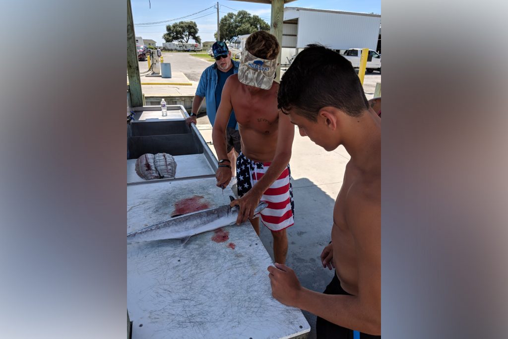 A cell phone image of three men back at the dock, filleting a fish after going fishing