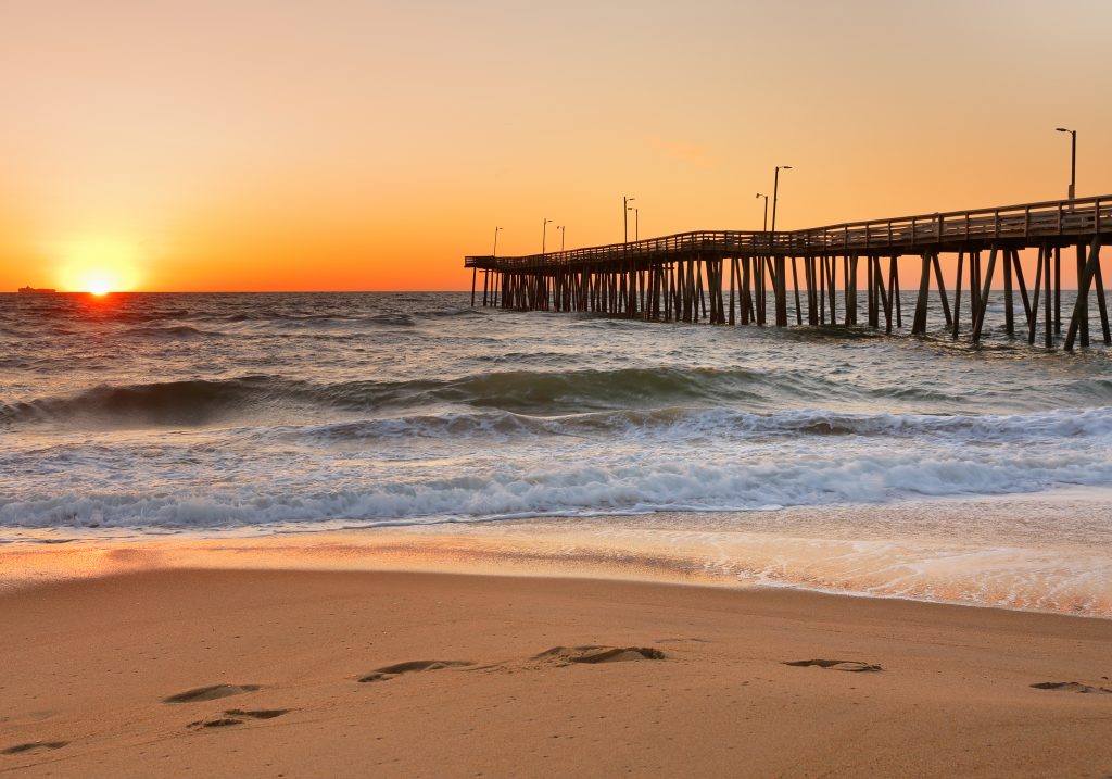 A view of Virginia Beach Fishing Pier at sunrise from the beach, with waves crashing in