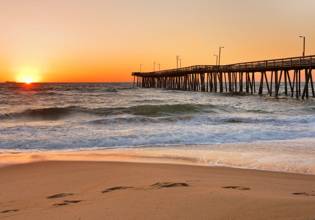 A view of Virginia Beach Fishing Pier at sunrise from the beach, with waves crashing in