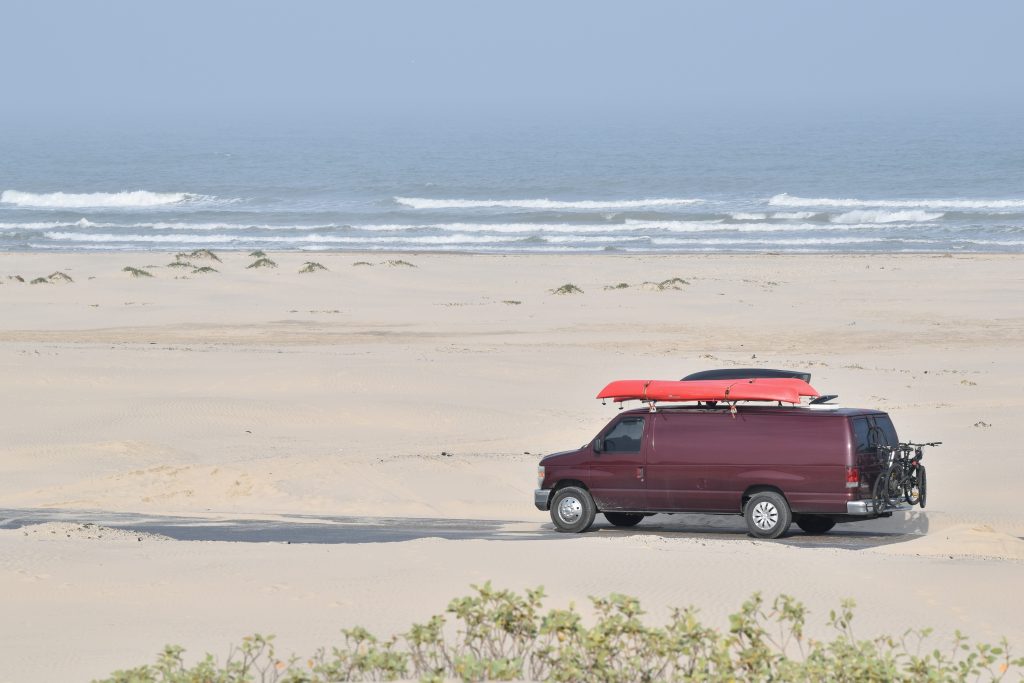 A van with kayaks on its roof driving along a beachside road on South Padre Island