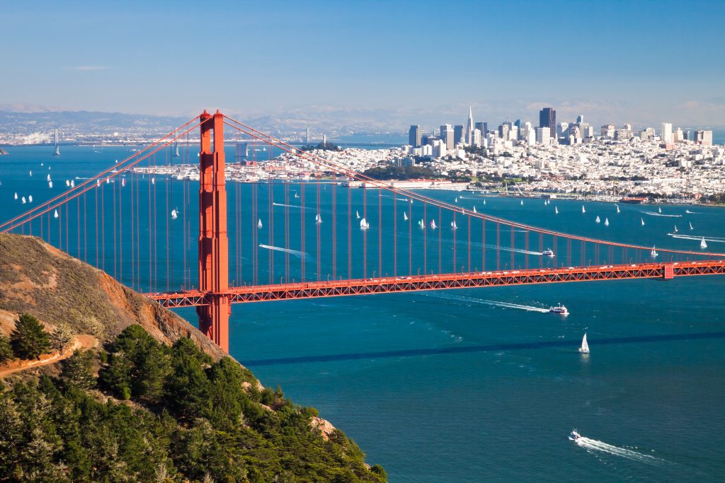 An aerial view of the Golden Gate Bridge, with boats in the bay and San Francisco in the distance