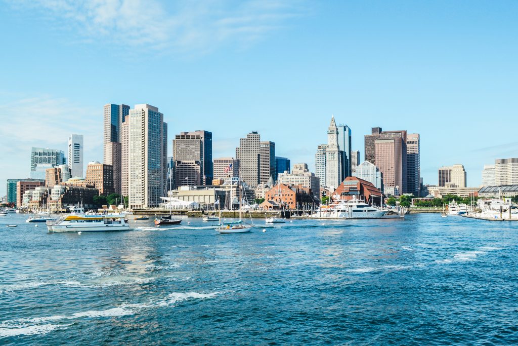 Boston Harbor seen from the water, with sailboats in the sea and the city skyline behind