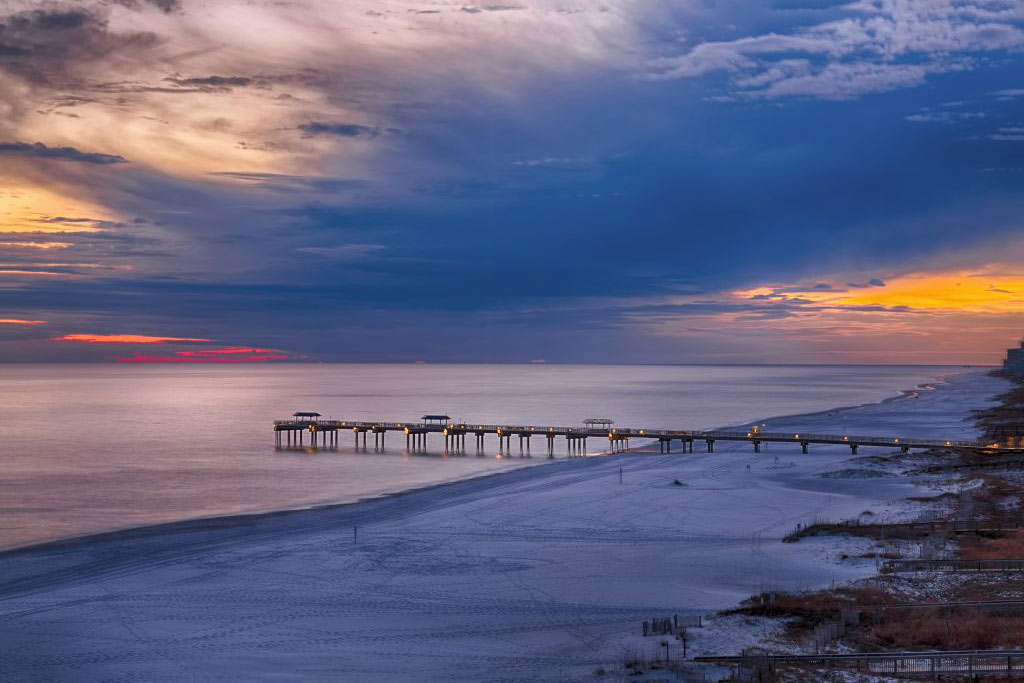 A sunset view of the beach, seas, and a fishing pier in Orange Beach, Alabama