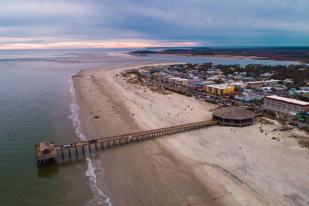 A view of a beach on Tybee Island, with a wooden pavilion on it and a fishing pier stretching out from it into the ocean