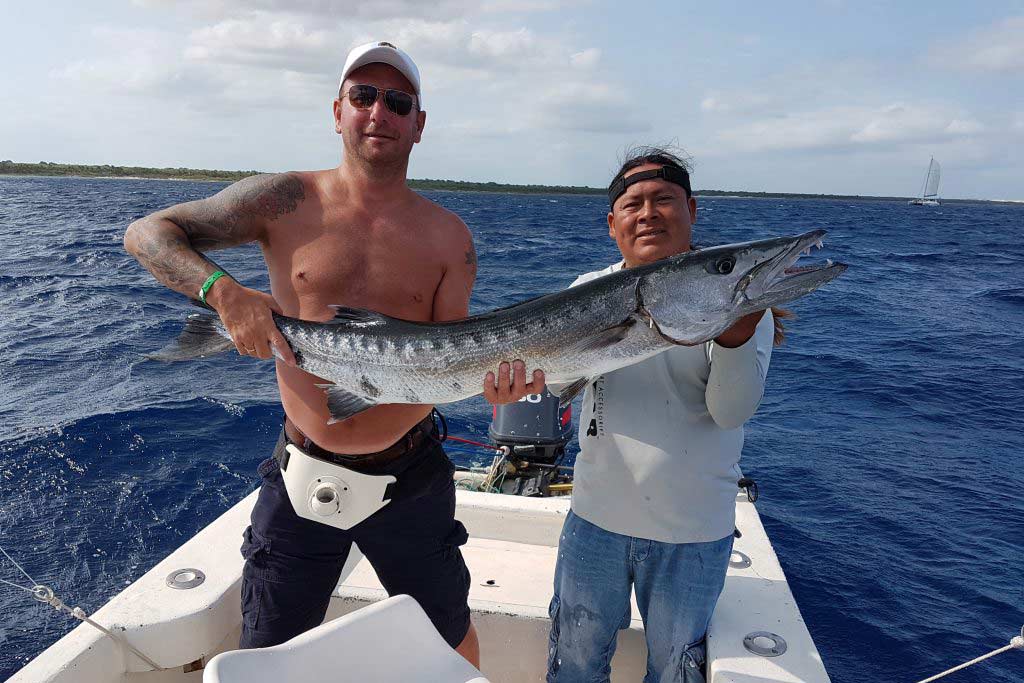 Two anglers standing on a boat, holding a huge Barracuda they caught fishing in Playa del Carmen during spring break