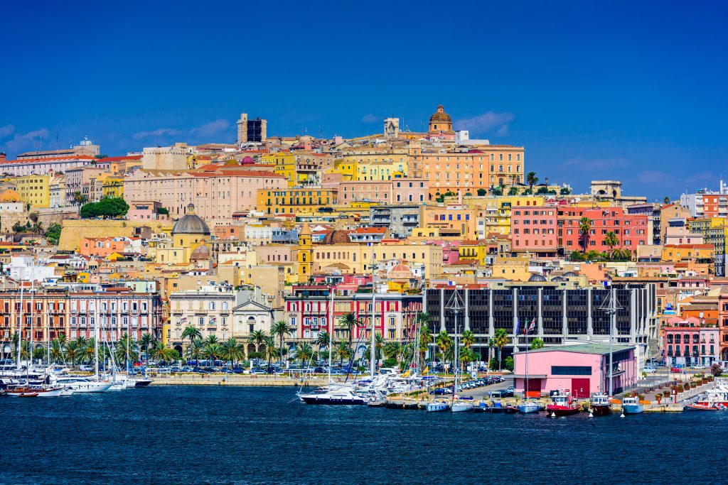 A view from the water of the city of Cagliari on Sardinia, with old buildings painted different colours and yachts moored in the harbour
