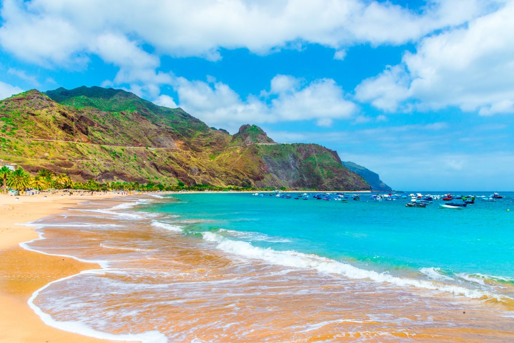 An idyllic beach on Tenerife, Canary Island, with yellow sand and small fishing boats in bright blue water, home to some of the best fishing in Europe