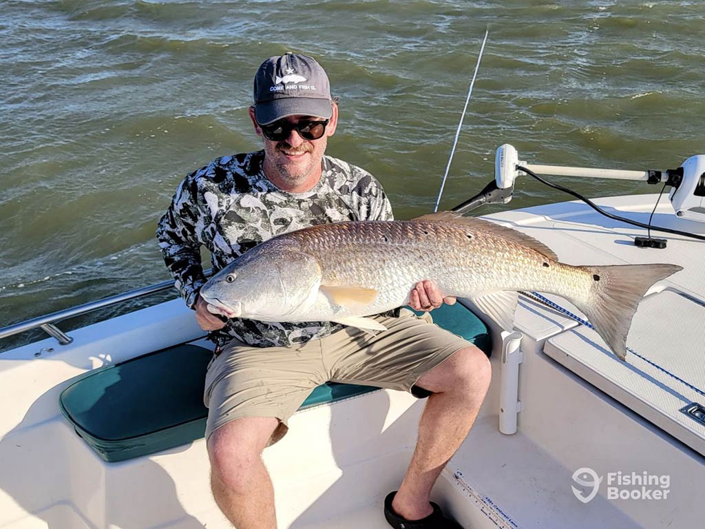 A man sitting on an inshore fishing boat in Galveston holding a large Redfish across his lap.