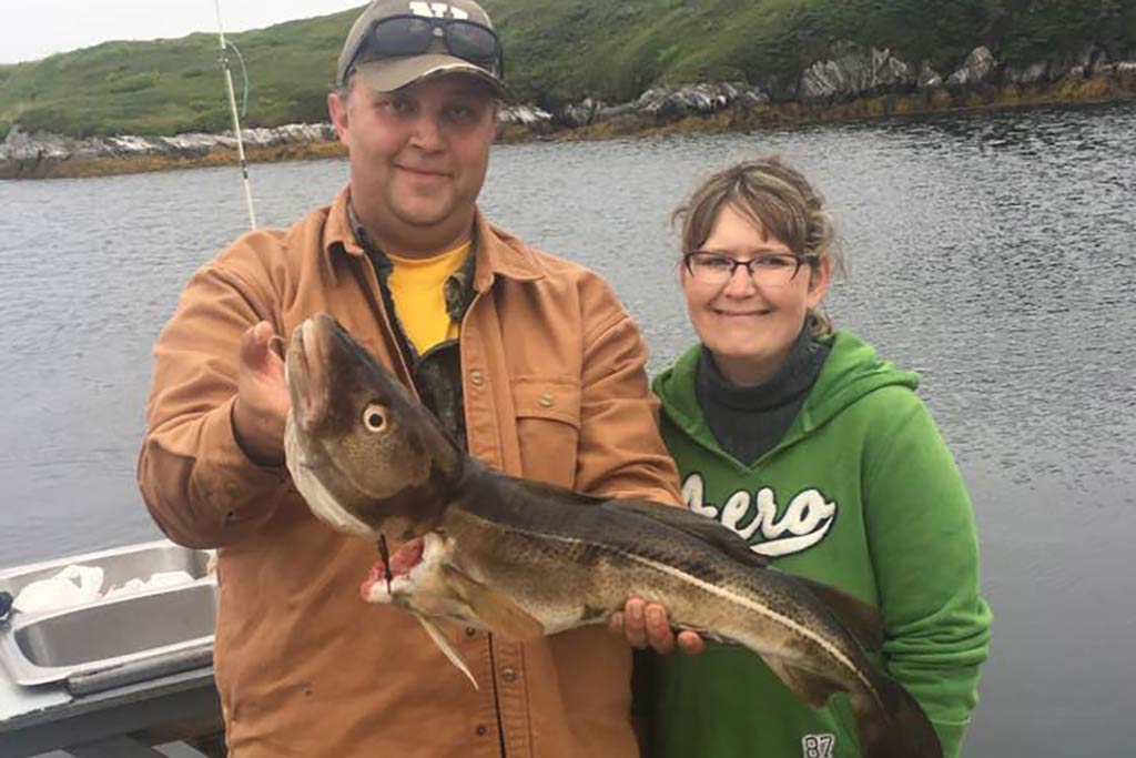 A man and a woman posing with their Cod catch on a cloudy day in Newfoundland