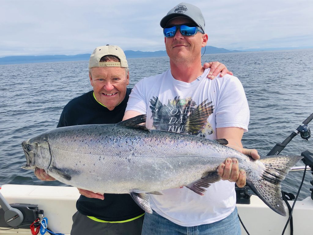 Two happy anglers holding a big Chinook Salmon