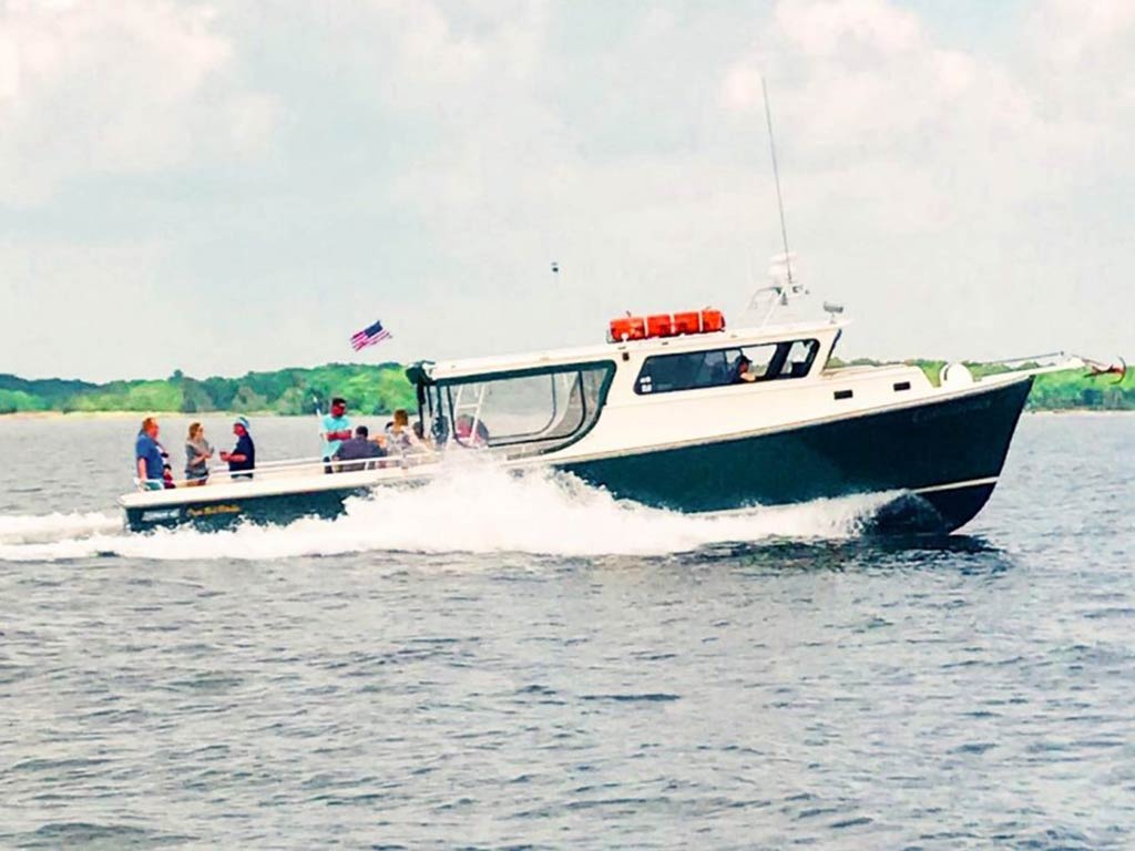 A picture of a party boat and its passengers cutting across the waves of a bay on the East Coast during a cloudy day
