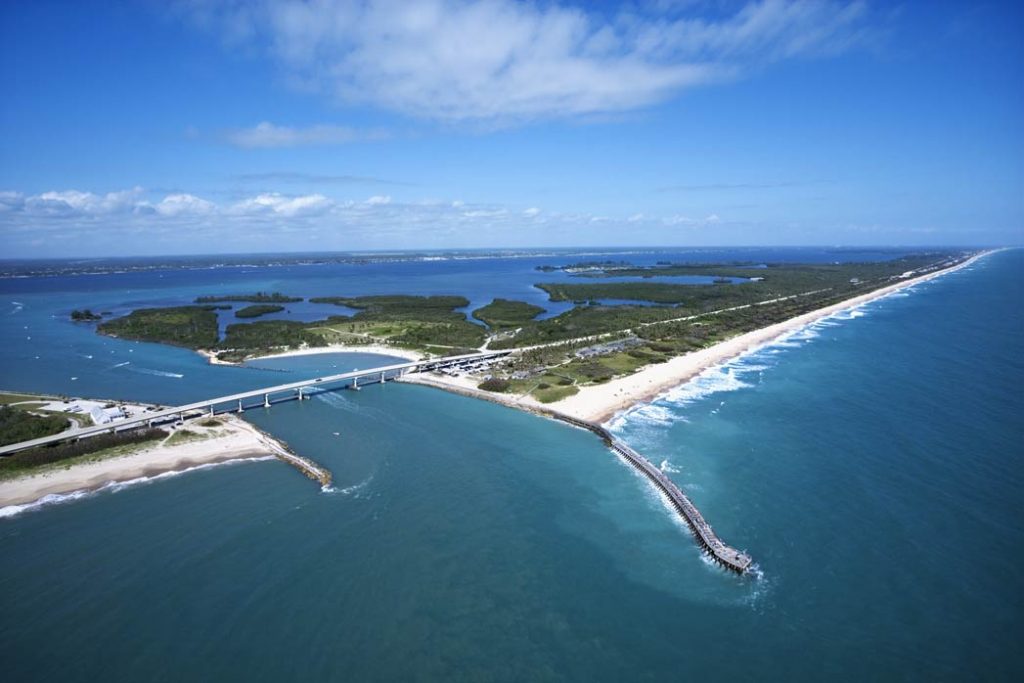 An aerial view of the Indian River, showing where it connects to an inlet, with a bridge over the inlet visible and a pier sticking out in the foreground