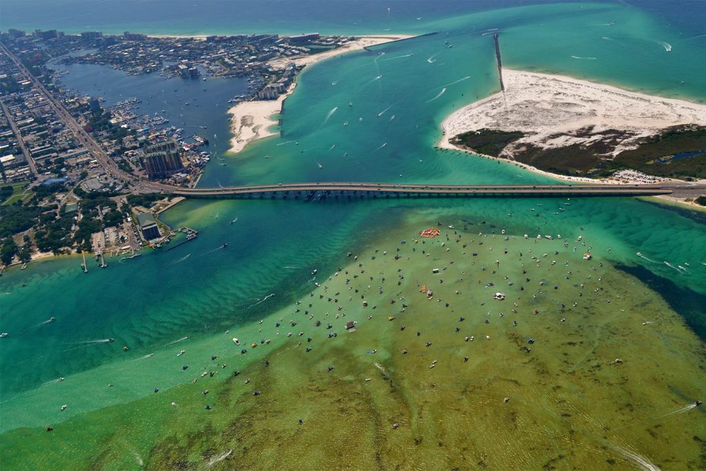 An aerial view of the Mid-Bay Bridge with destin on the left, surrounded by green waters full of boats