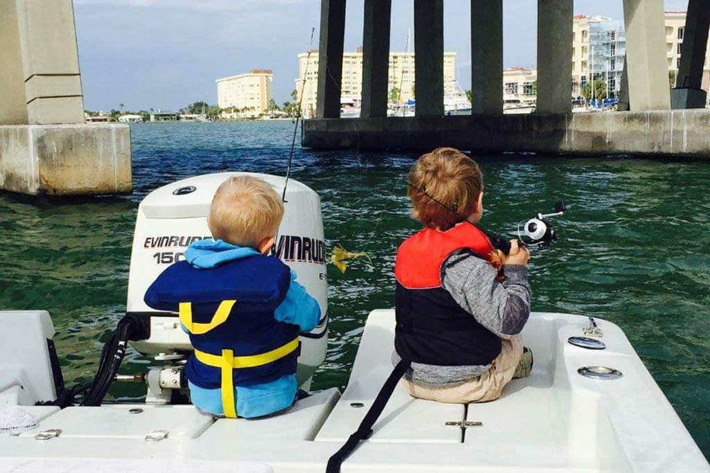 Two toddlers fishing from a boat with their backs turned to the camera