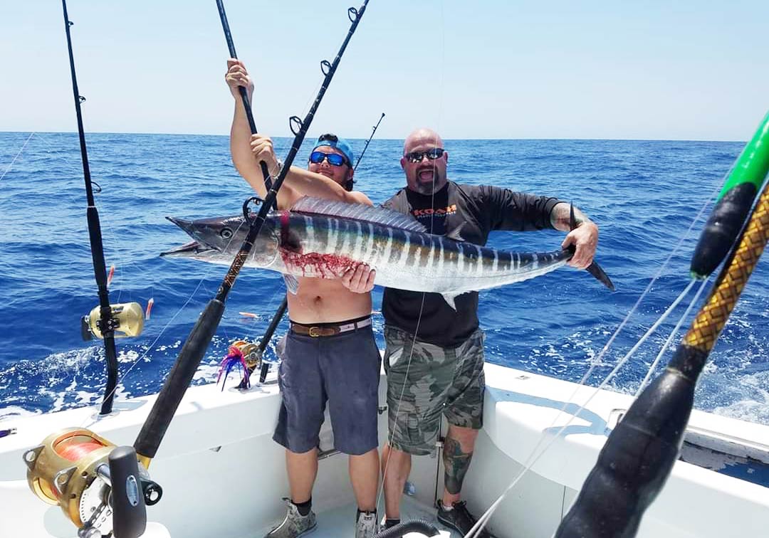 Two fishermen standing in the corner of a fishing boat, holding a citation Wahoo